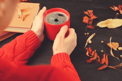 Photo of Woman with cup of hot drink at black table, closeup. Cozy autumn atmosphere