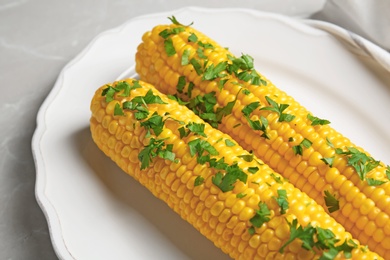 Plate with delicious boiled corn cobs and parsley on light table