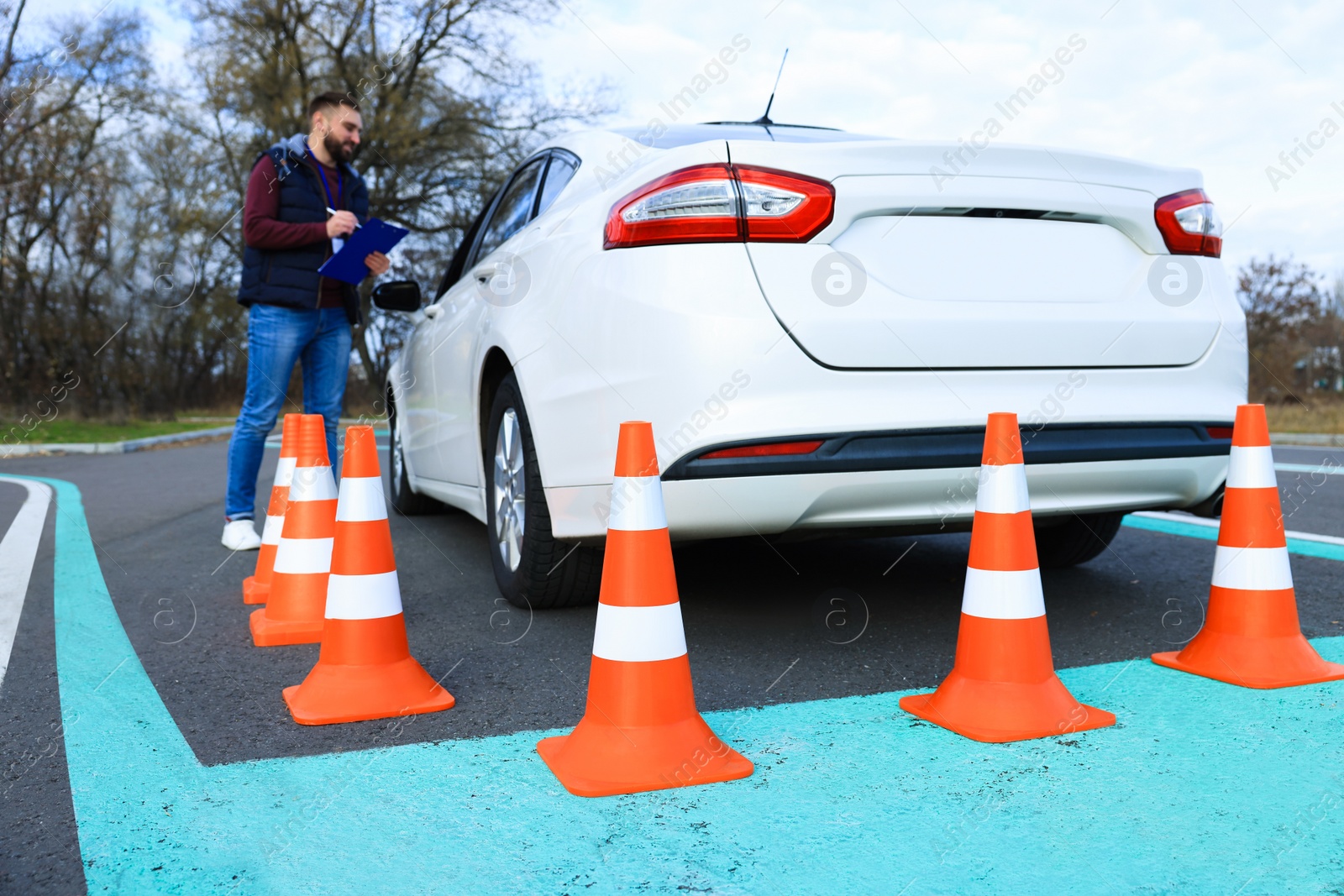 Photo of Instructor near car with student during exam at driving school test track, focus on traffic cones