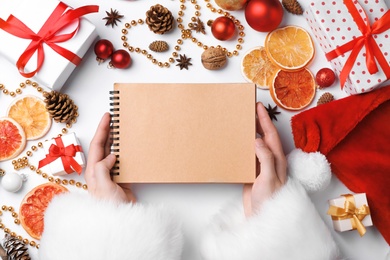 Santa Claus holding notebook and Christmas decor on white background, top view