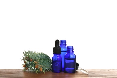 Bottles of essential oil, pipette and pine branch on table against white background