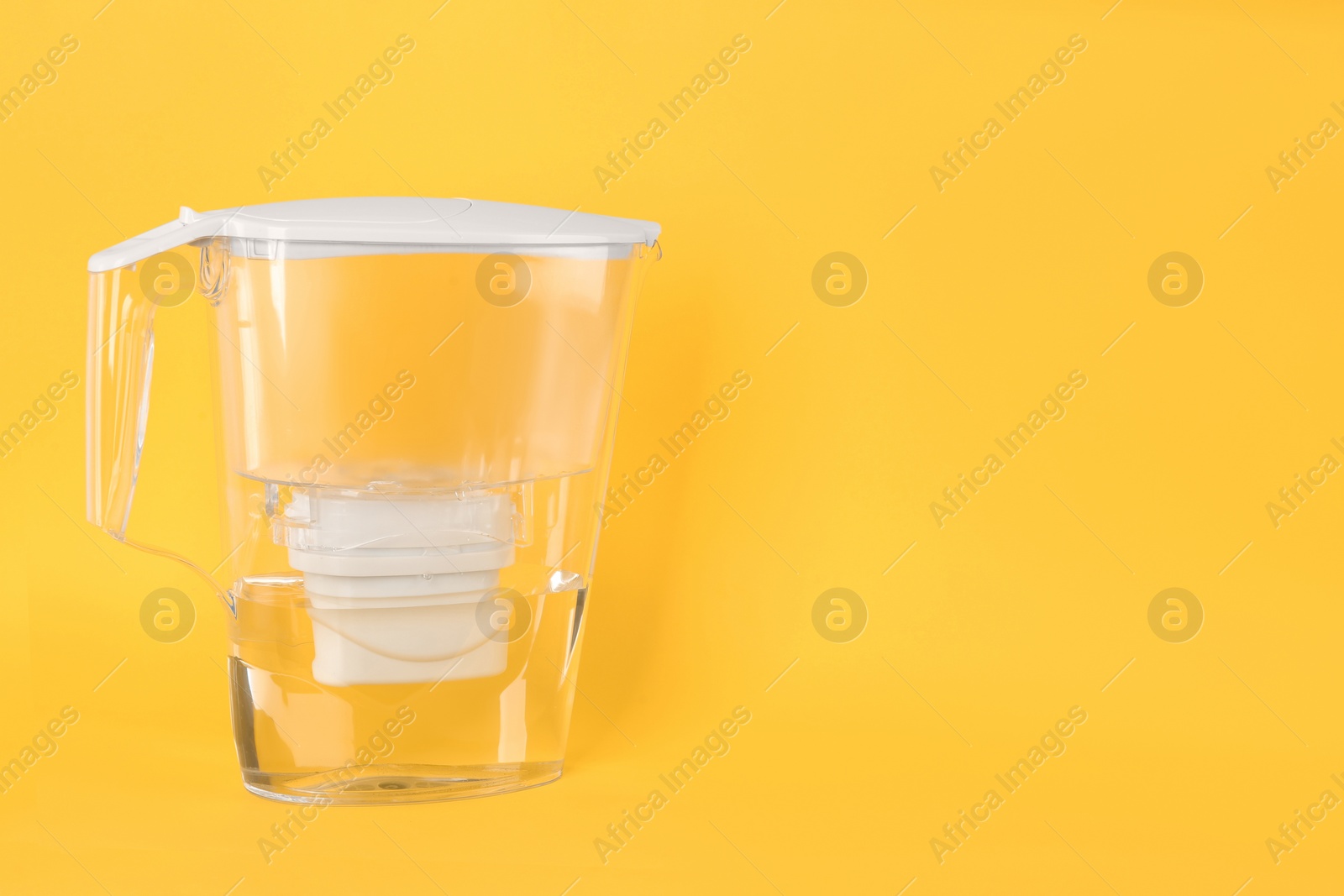 Photo of Filter jug with purified water on yellow background. Space for text