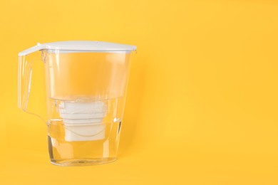 Photo of Filter jug with purified water on yellow background. Space for text