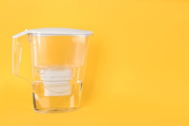 Filter jug with purified water on yellow background. Space for text