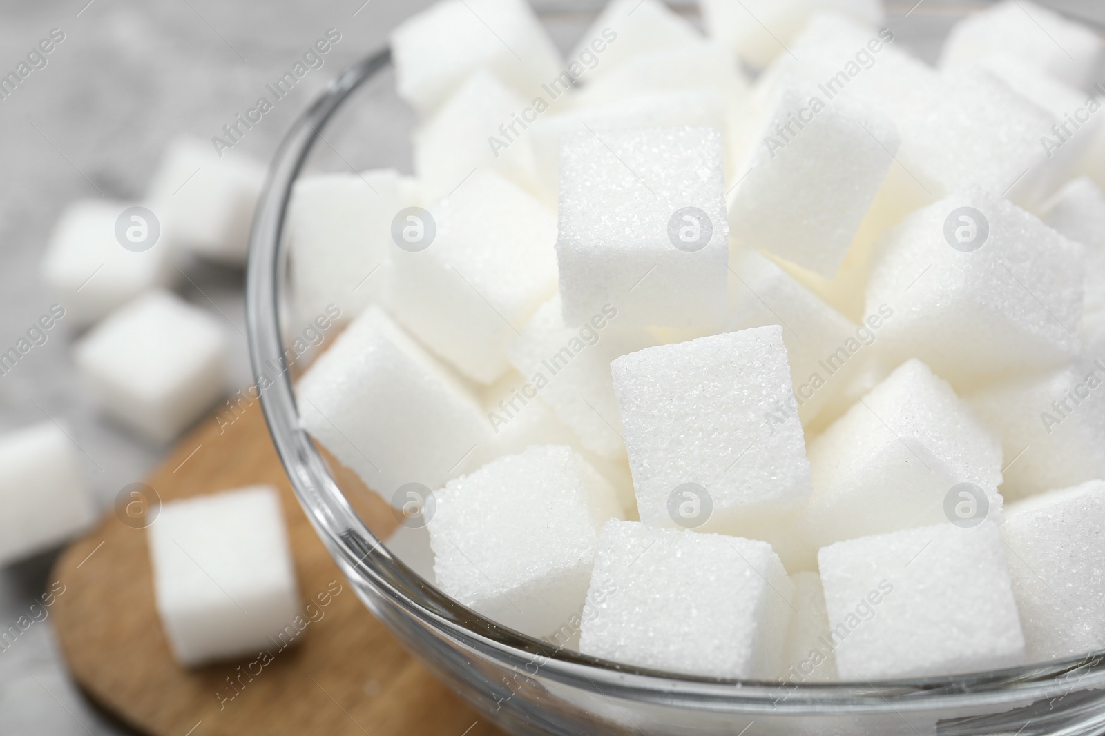 Photo of White sugar cubes in glass bowl on grey table, closeup