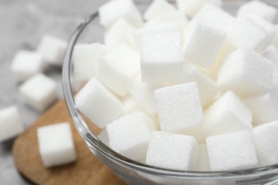 Photo of White sugar cubes in glass bowl on grey table, closeup