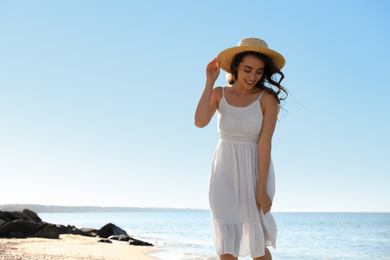 Happy young woman with hat on beach near sea. Space for text