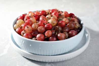 Photo of Bowl full of ripe gooseberries on light grey marble table, closeup