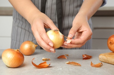 Photo of Young woman peeling ripe onion at grey table, closeup