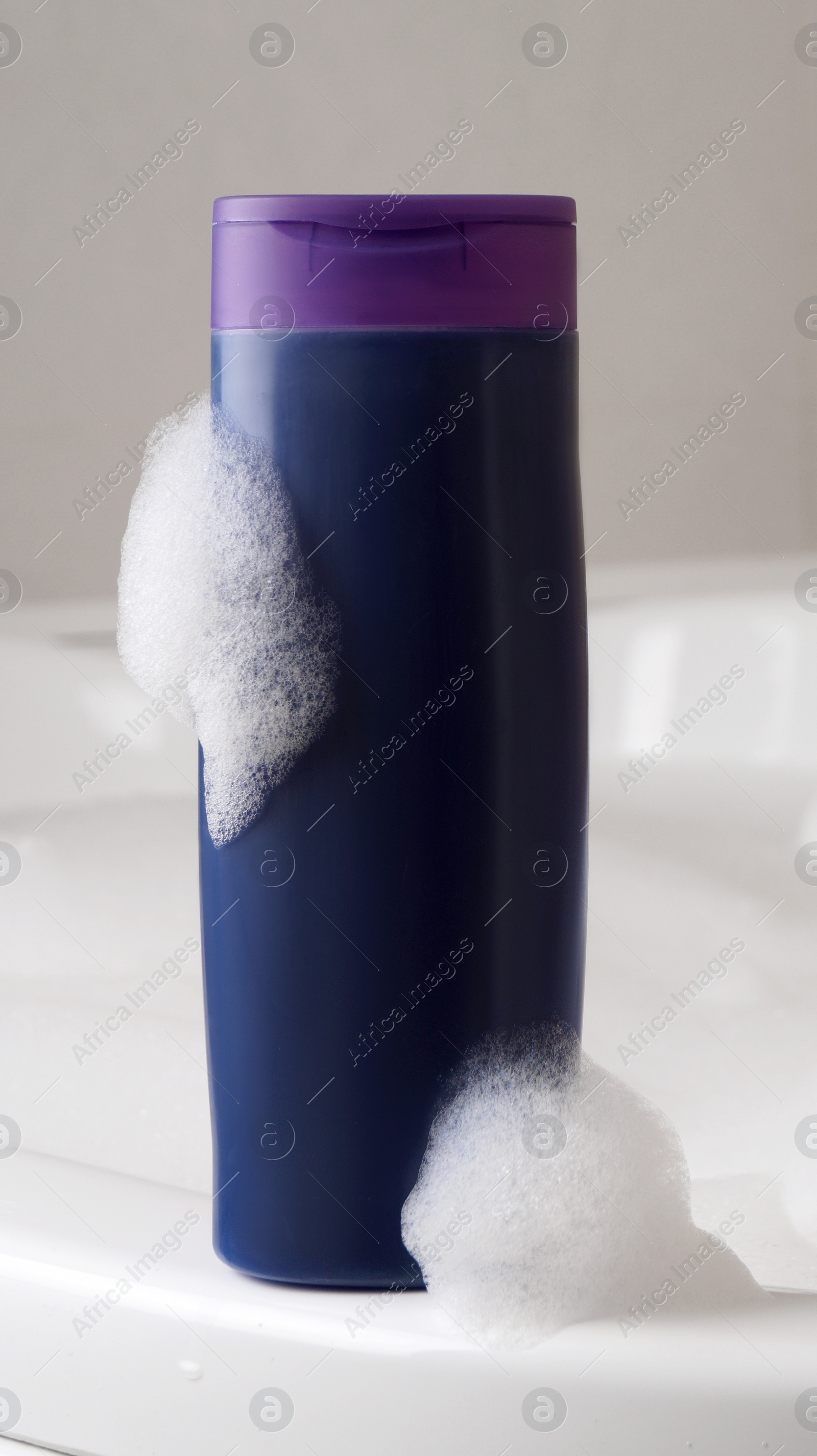 Purple bottle of bubble bath with foam on tub indoors Photo of Purple bottle of bubble bath with foam on tub indoors