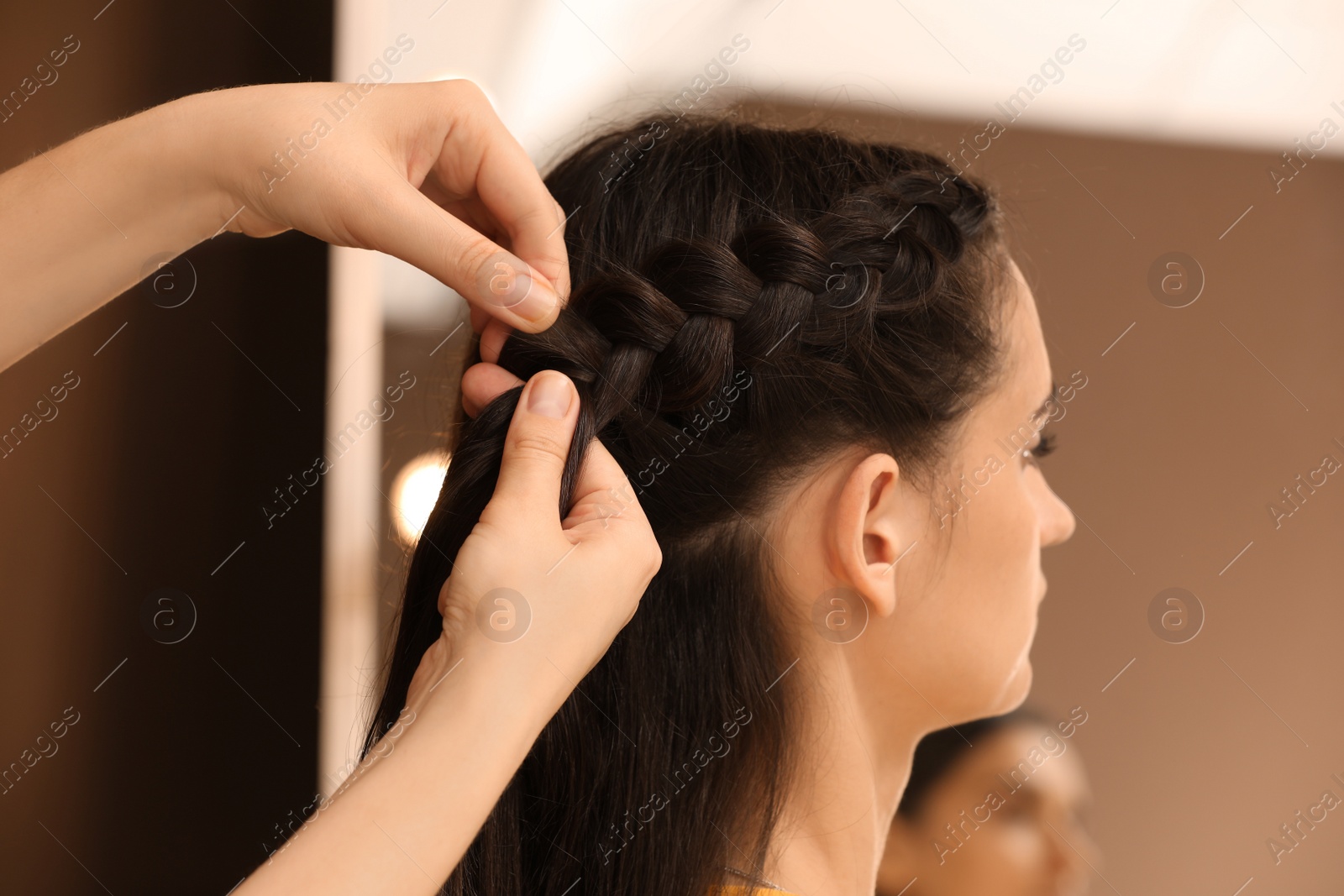 Photo of Professional stylist braiding client's hair in salon