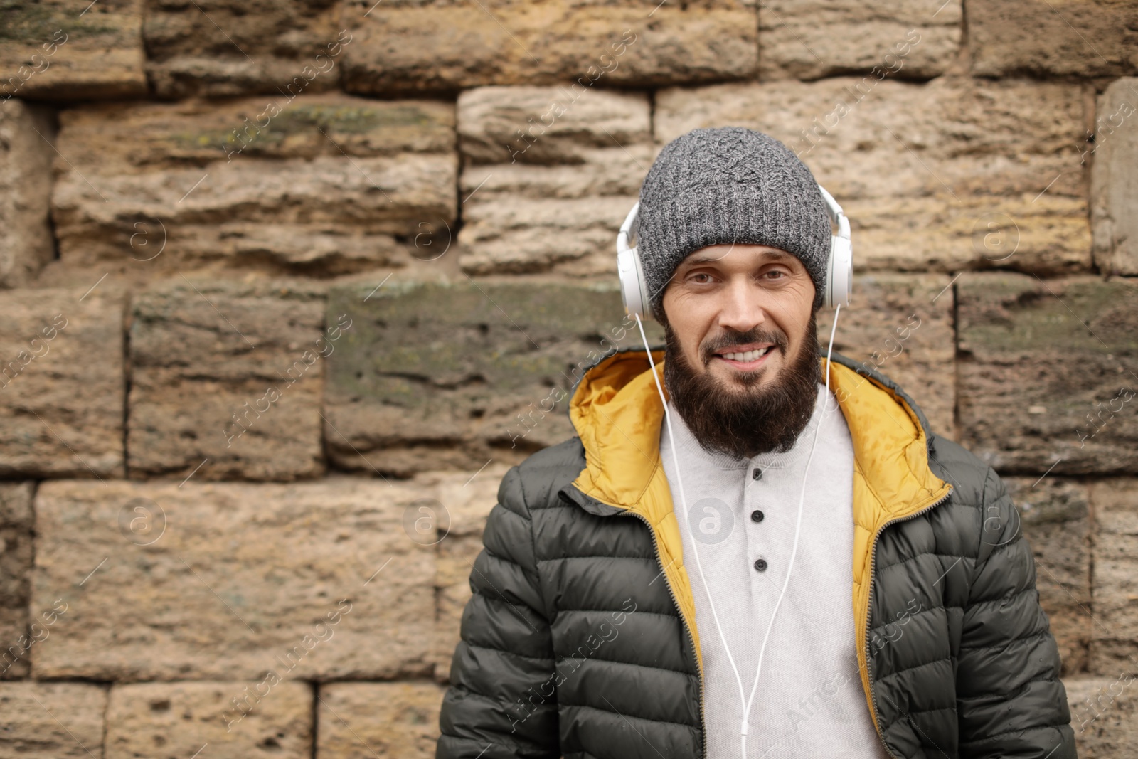 Photo of Mature man with headphones listening to music near stone wall. Space for text