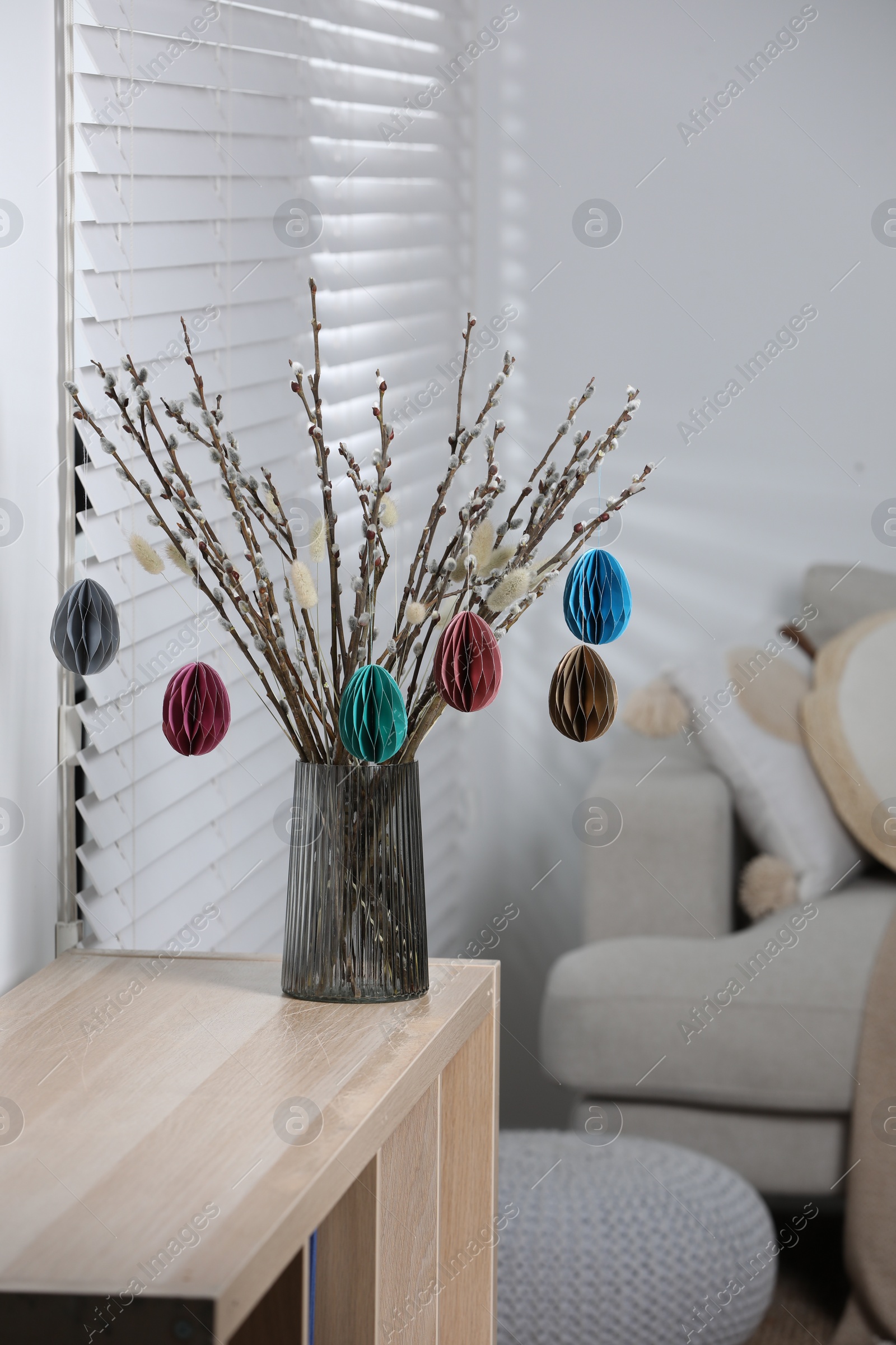 Photo of Beautiful pussy willow branches with paper eggs in vase on shelving unit at home. Easter decor