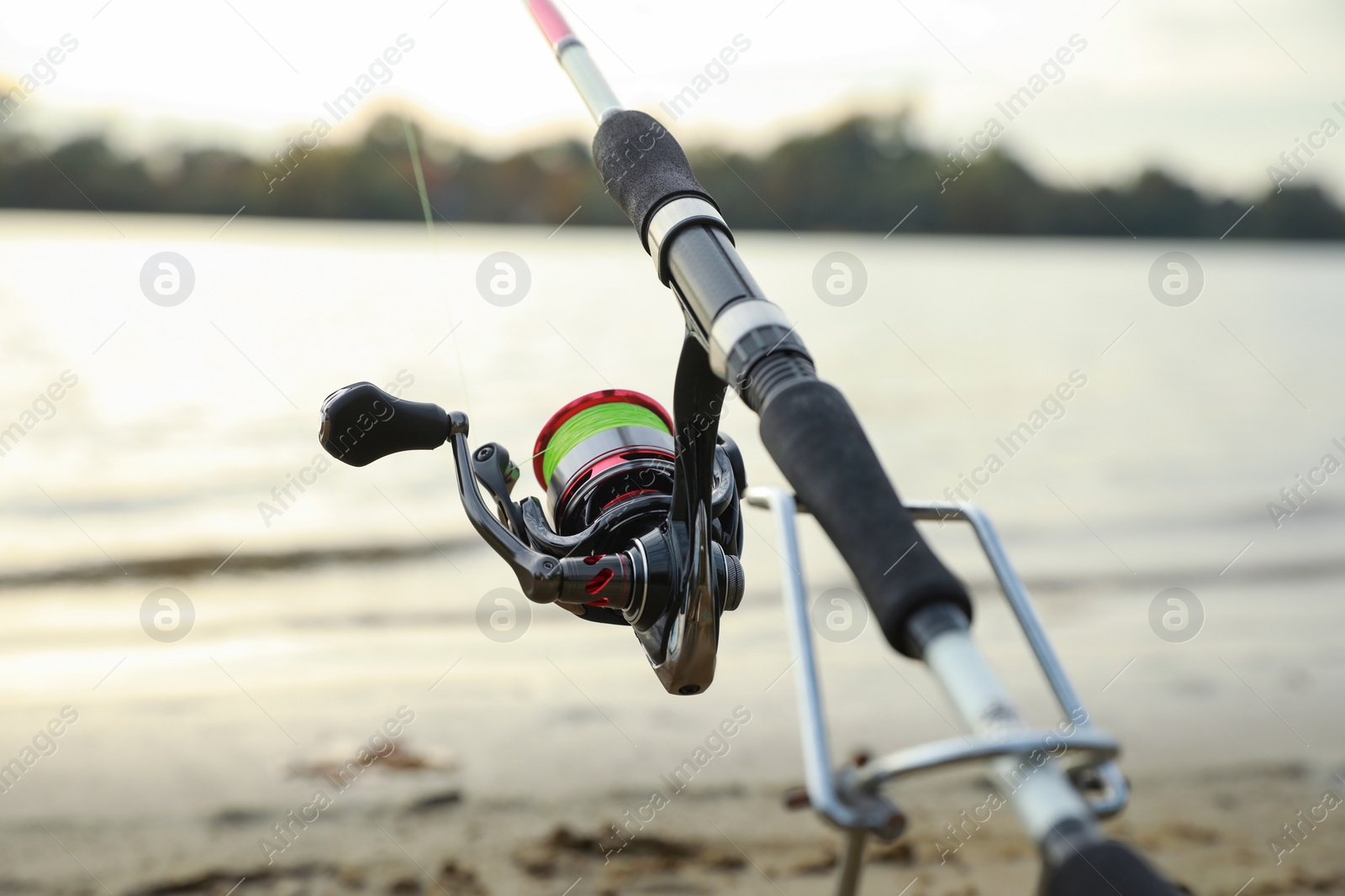 Photo of Fishing rod with reel near river, closeup