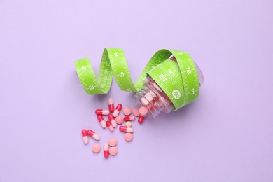 Photo of Jar of weight loss pills and measuring tape on violet background, flat lay
