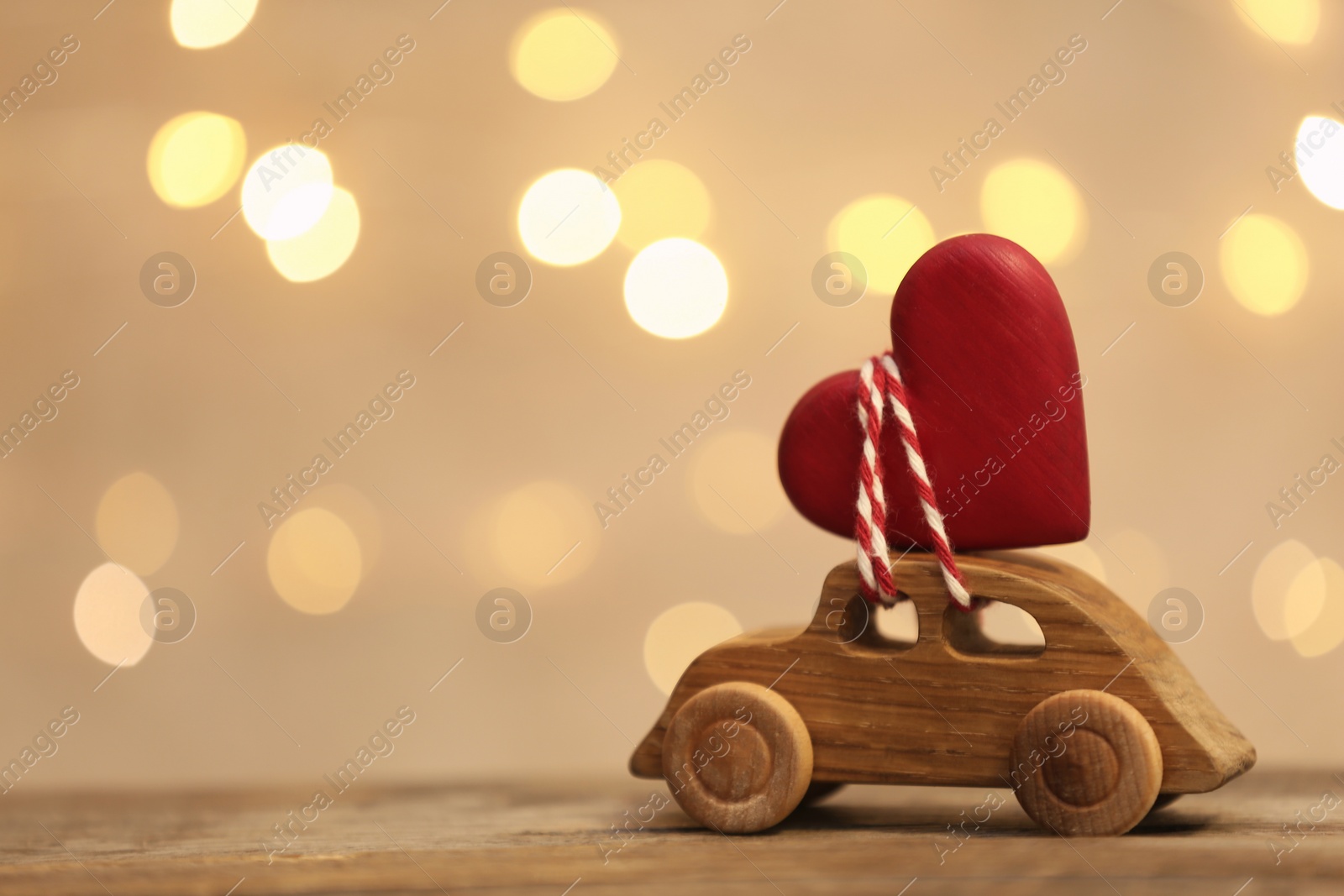 Photo of Toy car with red heart on table against blurred lights. Space for text