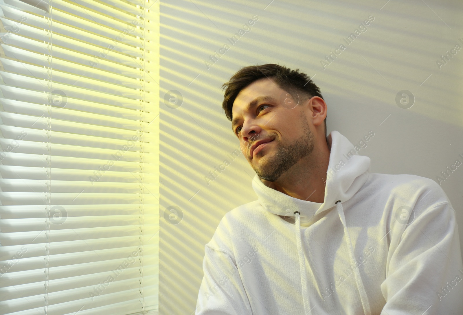 Photo of Handsome man near window with Venetian blinds. Space for text