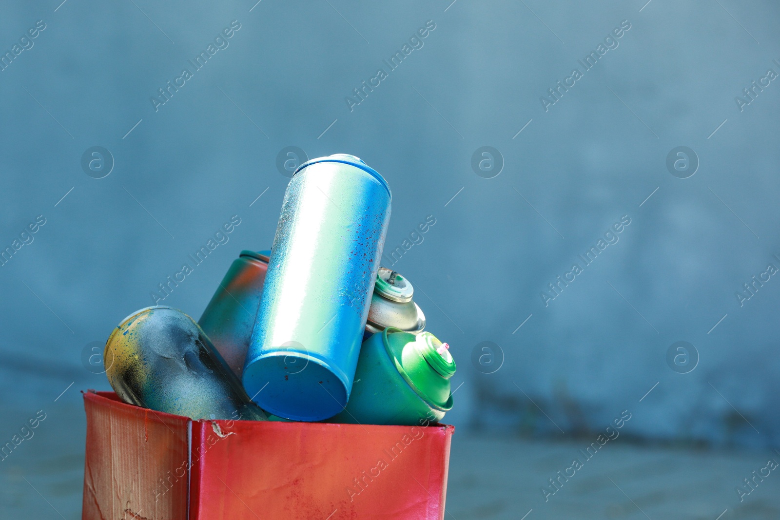 Photo of Many spray paint cans and red cardboard box outdoors, closeup. Space for text