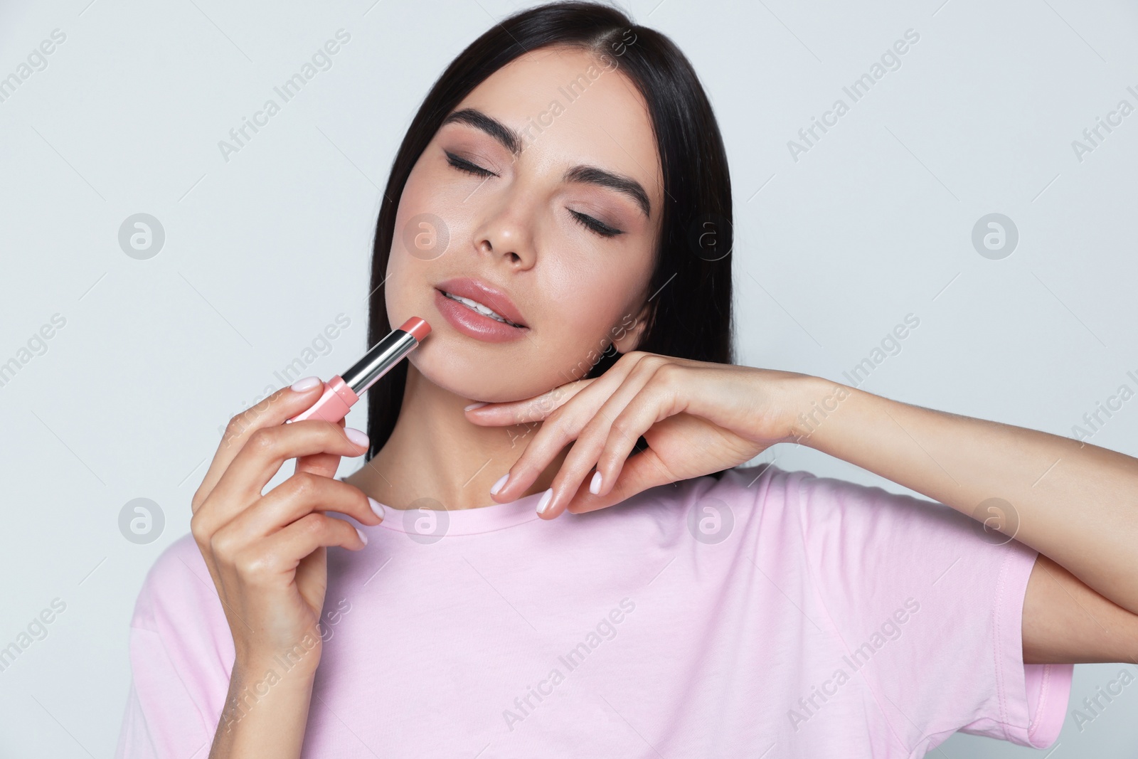 Photo of Young woman with beautiful makeup holding nude lipstick on light gray background