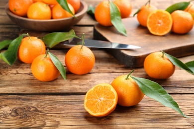 Photo of Fresh ripe tangerines with green leaves on wooden table