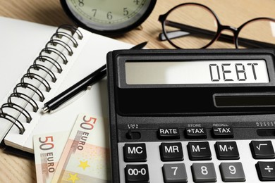 Calculator with word Debt and money on wooden table, closeup