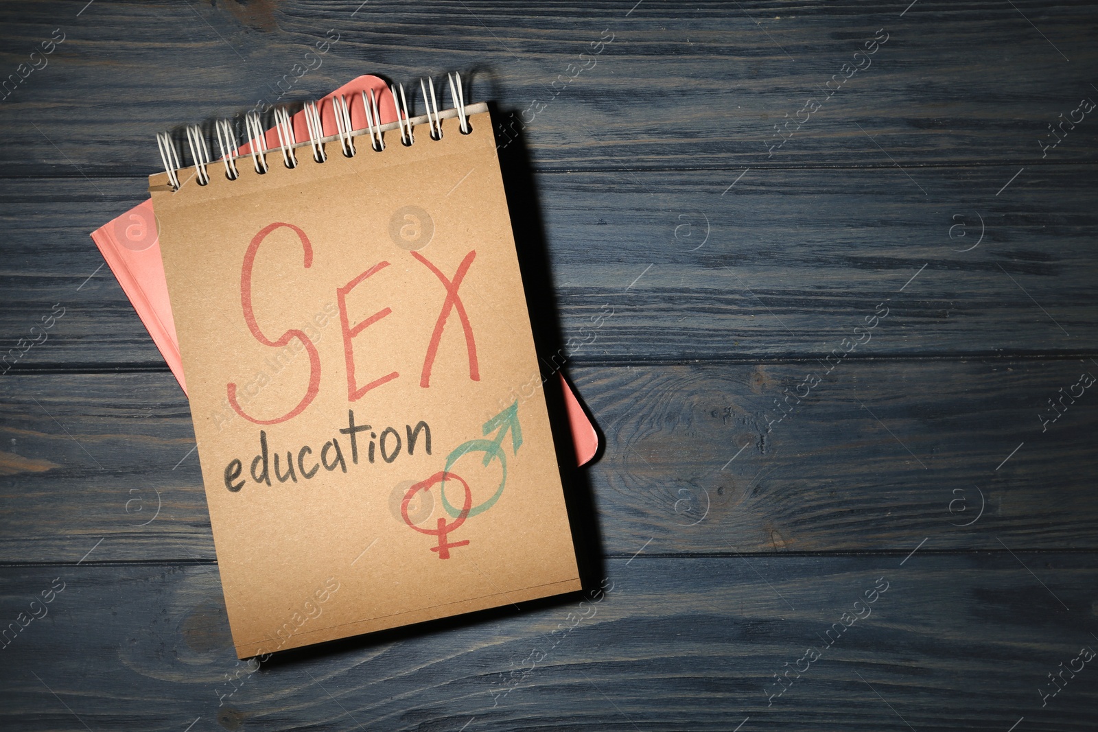 Photo of Notebook with phrase "SEX EDUCATION" and gender symbols on dark wooden background, top view. Space for text