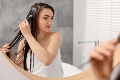 Photo of Young woman applying hair mask near mirror in bathroom