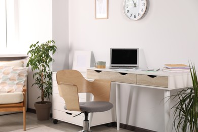 Photo of Beautiful workplace with laptop on white wooden table, chair and decor elements in room