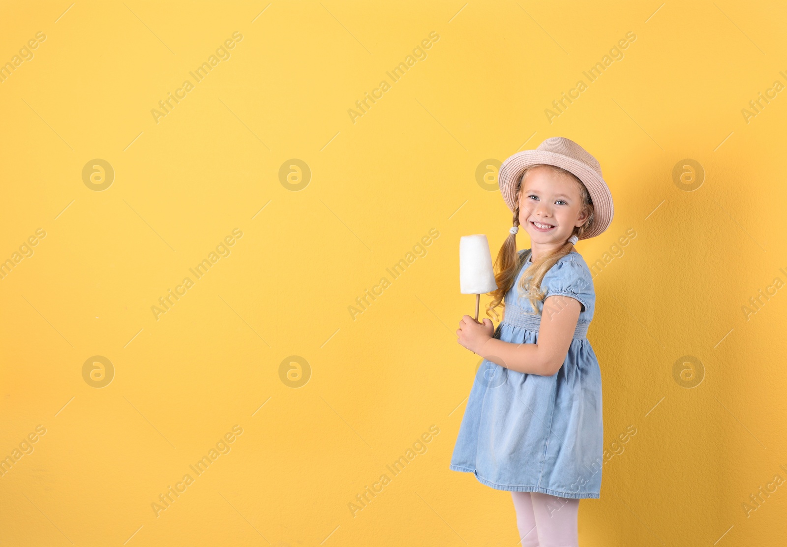 Photo of Cute little girl with cotton candy on color background. Space for text