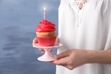 Photo of Woman holding stand with birthday cupcake on blurred background