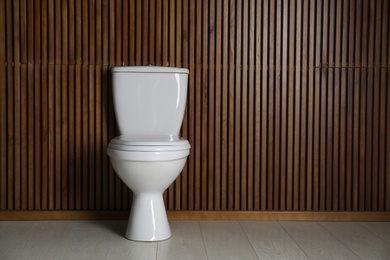 Photo of New toilet bowl near wooden wall indoors. Space for text