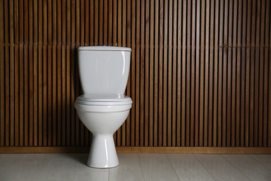 New toilet bowl near wooden wall indoors. Space for text