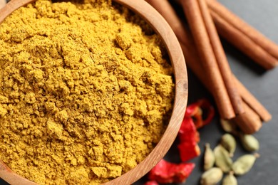 Dry curry powder in bowl and other spices on dark table, flat lay