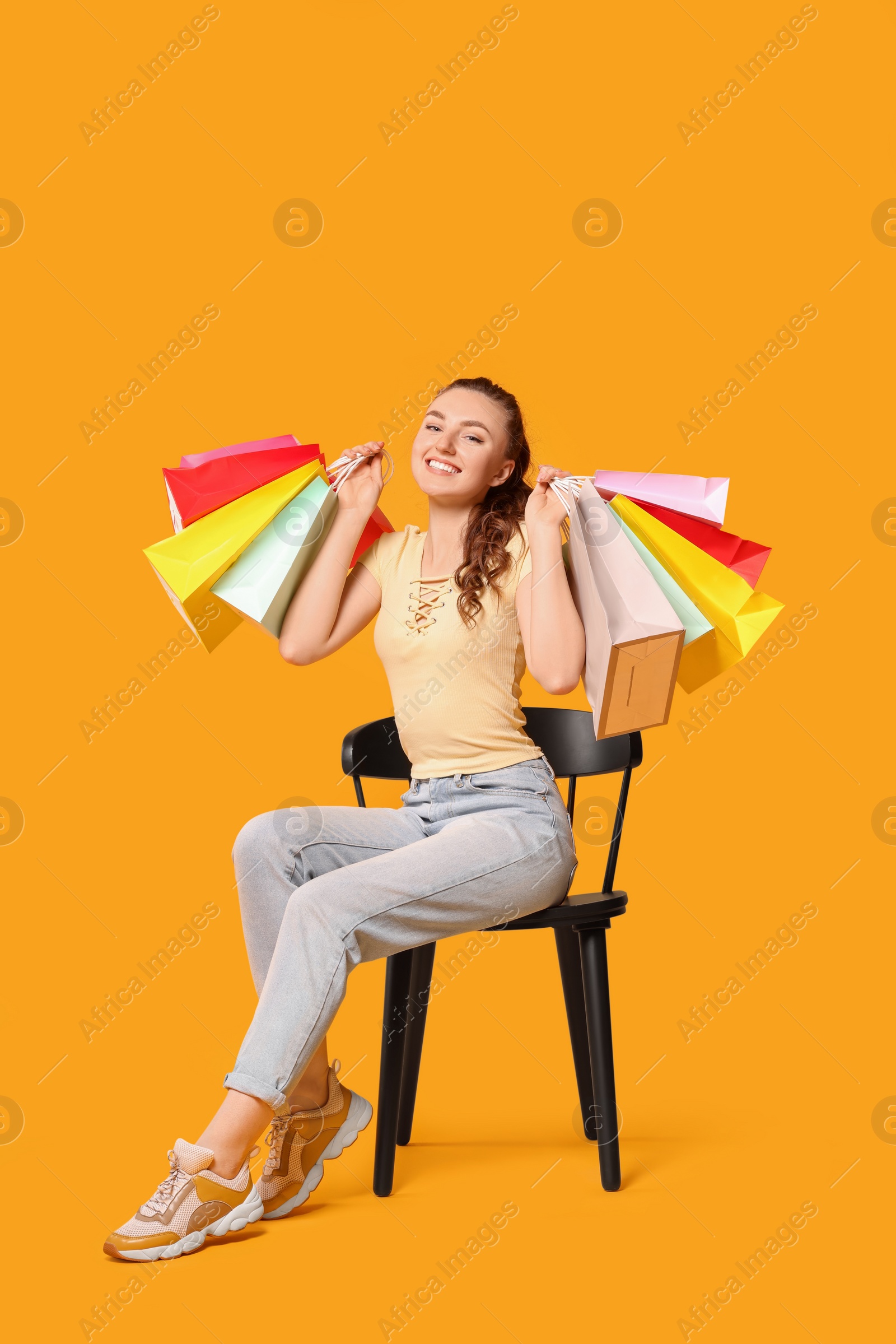 Photo of Happy woman holding colorful shopping bags on chair against orange background