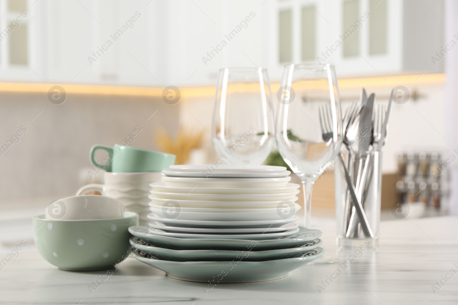 Photo of Many different clean dishware and glasses on white marble table in kitchen