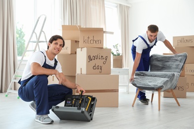Photo of Male movers with instruments and armchair in new house