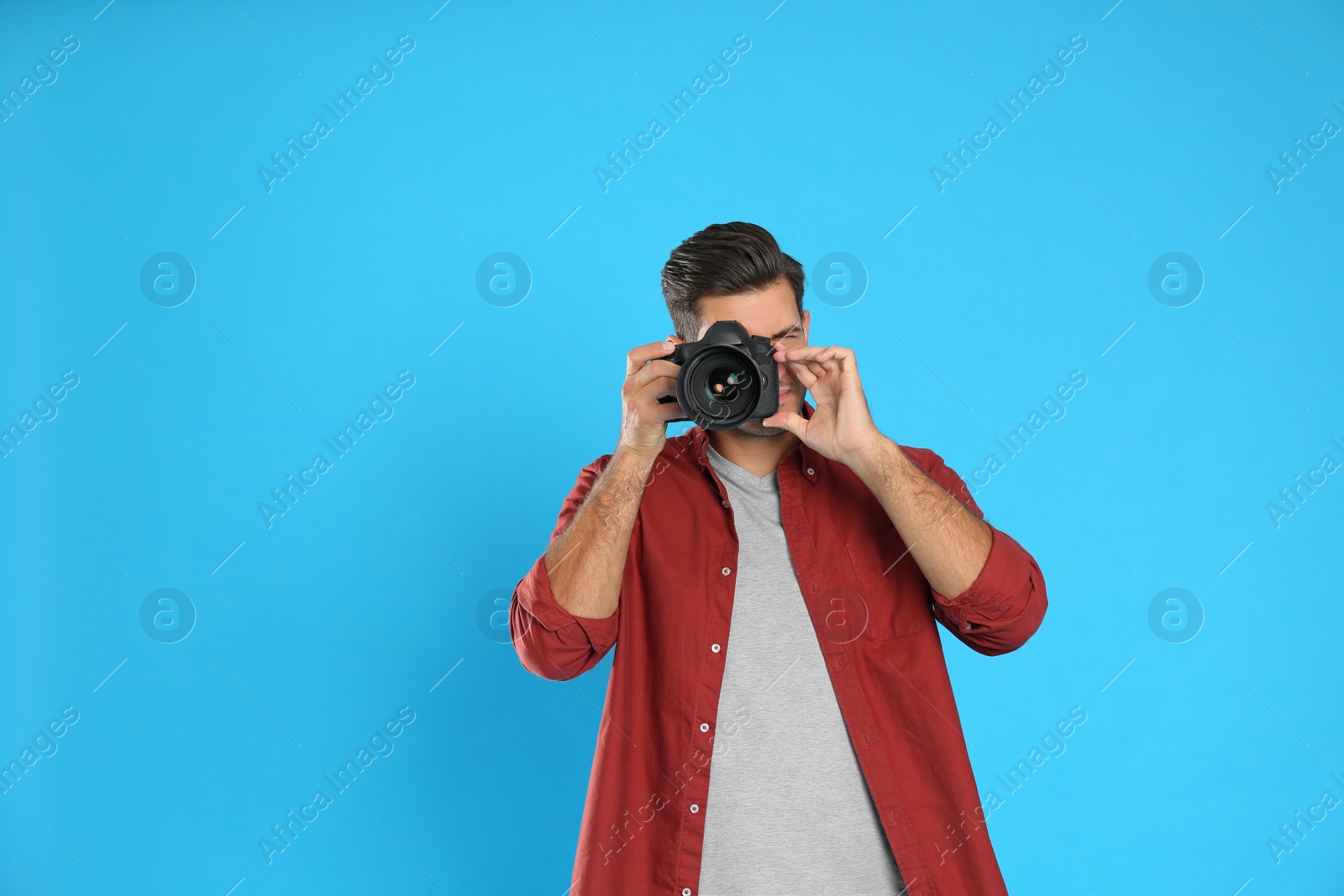 Photo of Professional photographer working on light blue background in studio. Space for text