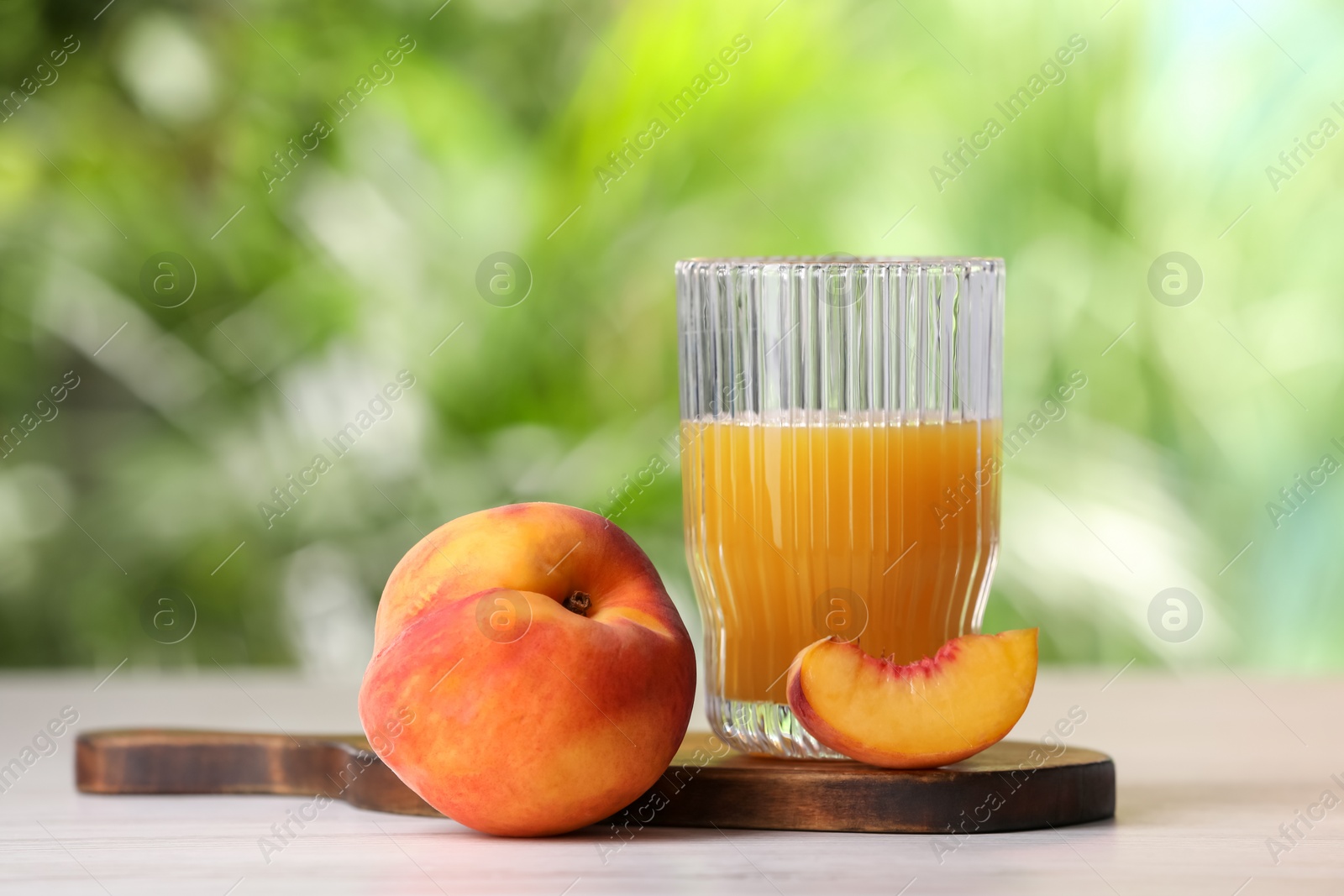 Photo of Glass of tasty peach juice and fresh fruits on white wooden table outdoors, closeup