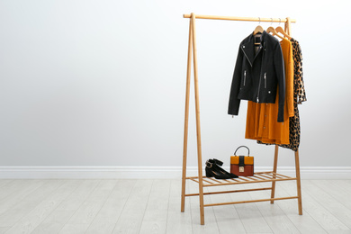 Photo of Wooden rack with stylish clothes in room. Space for text