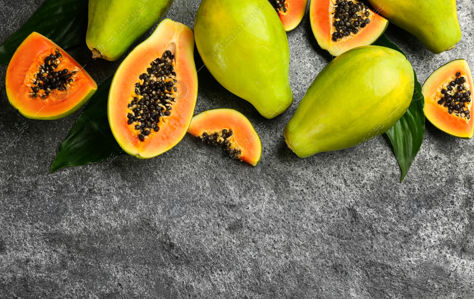 Photo of Fresh ripe papaya fruits with green leaves on grey table, flat lay. Space for text