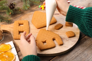 Photo of Woman making gingerbread house at wooden table, closeup