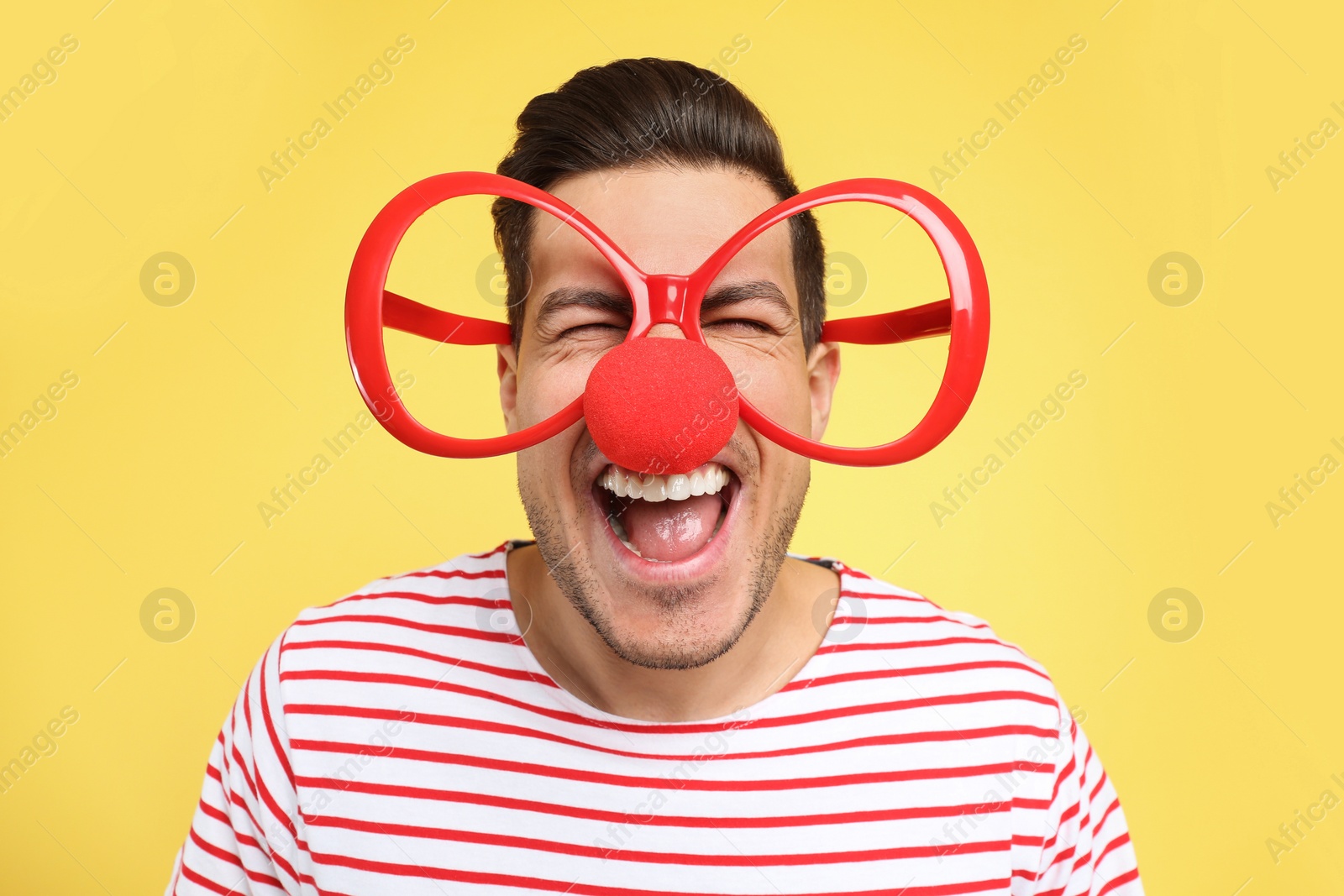 Photo of Funny man with clown nose and large glasses on yellow background. April fool's day