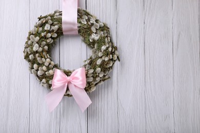 Wreath made of beautiful willow branches and pink bow hanging on white wooden background. Space for text