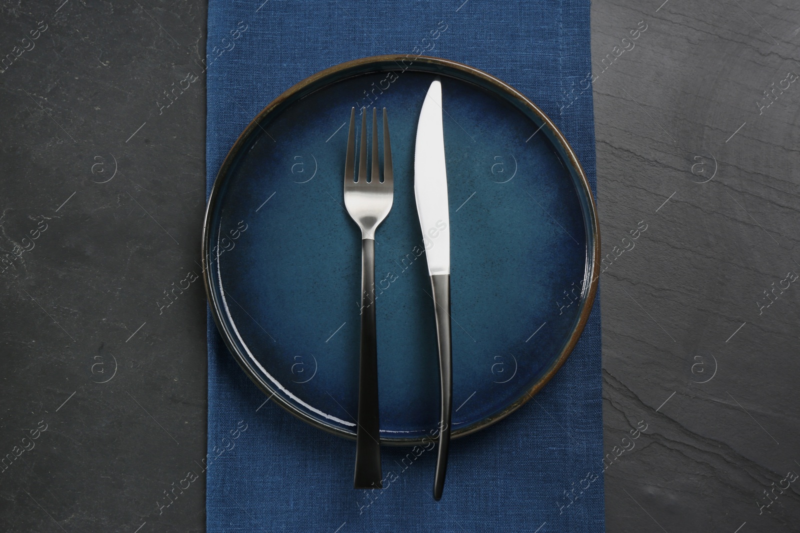 Photo of Ceramic plate, fork and knife on black table, top view