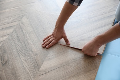 Worker installing laminated wooden floor indoors, closeup