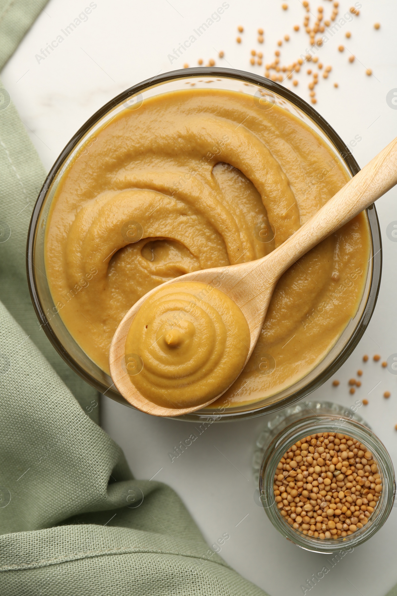 Photo of Tasty mustard sauce and dry seeds on white table, flat lay
