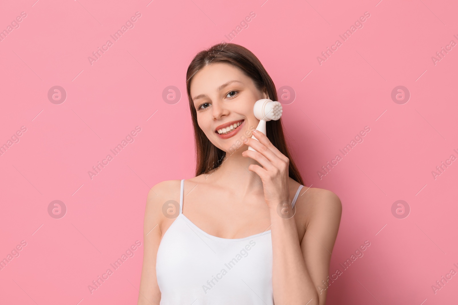 Photo of Washing face. Young woman with cleansing brush on pink background