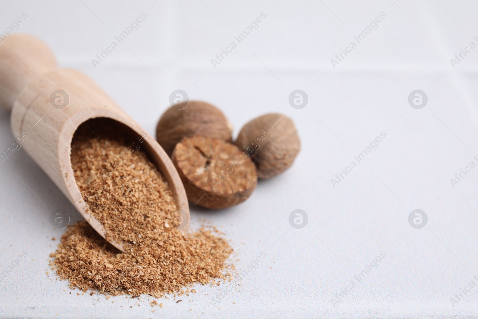 Photo of Scoop with grated nutmeg and seeds on white table, closeup. Space for text