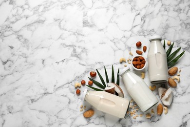 Vegan milk and different nuts on white marble table, flat lay. Space for text