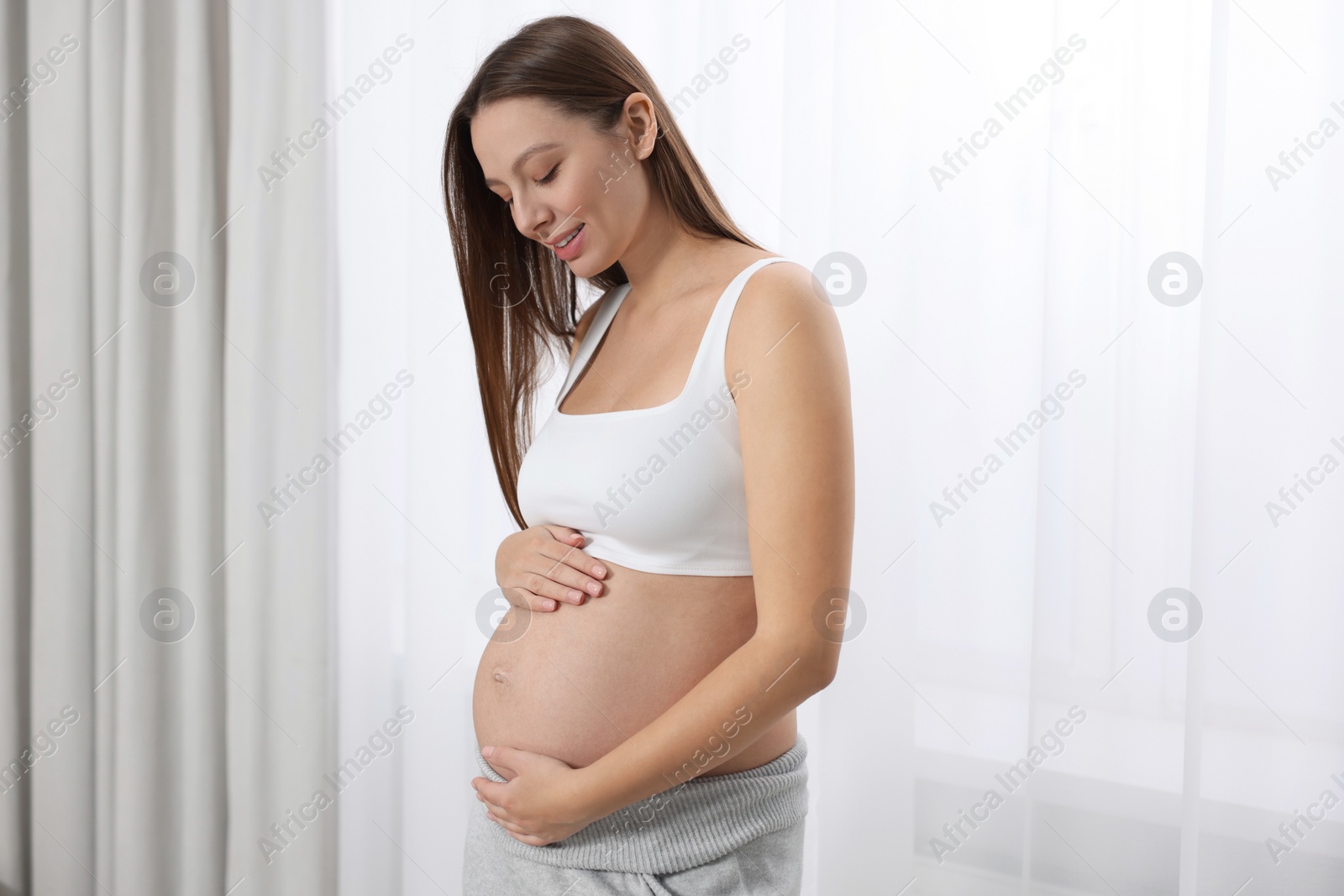 Photo of Beautiful pregnant woman with long hair near window indoors